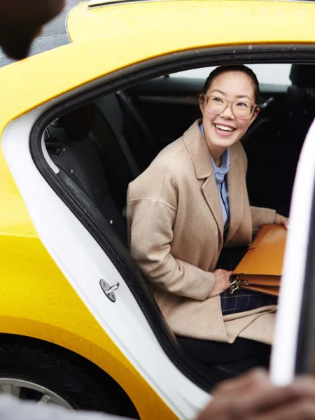 Professional photo of a taxi driver helping a young woman out of the back of a yellow taxi cab